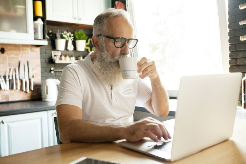 old man sitting in his kitchen working from his laptop
